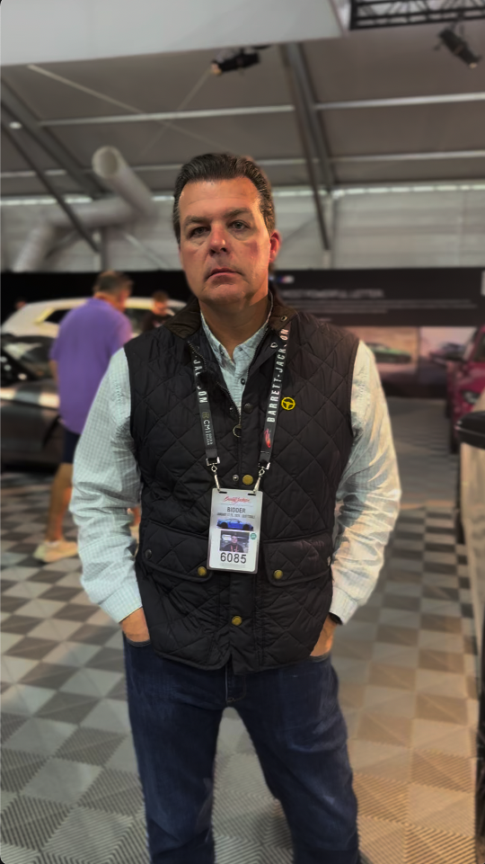 Man wearing a black quilted vest and event badge stands indoors.