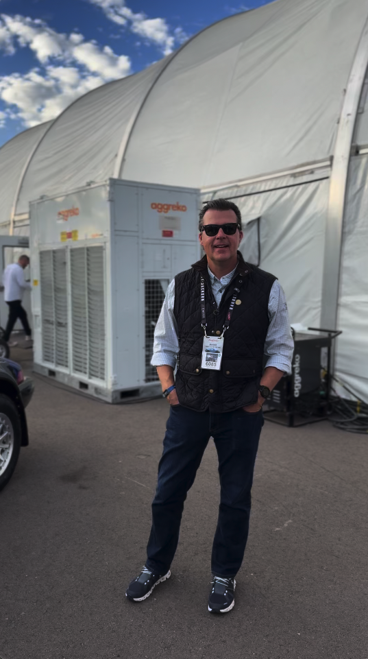 Man wearing sunglasses and a vest standing outdoors near a tent.