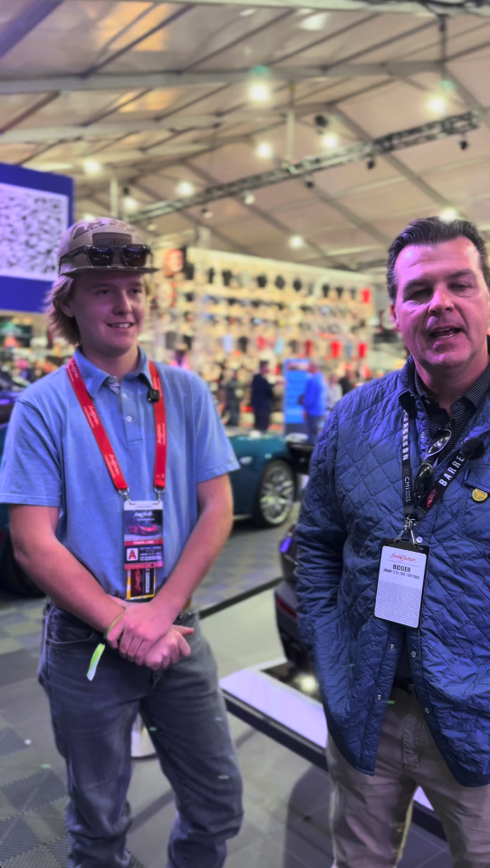 Two men smiling at a bustling event with badges and lanyards.