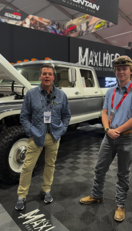 Two men standing and smiling at a vehicle exhibit booth.